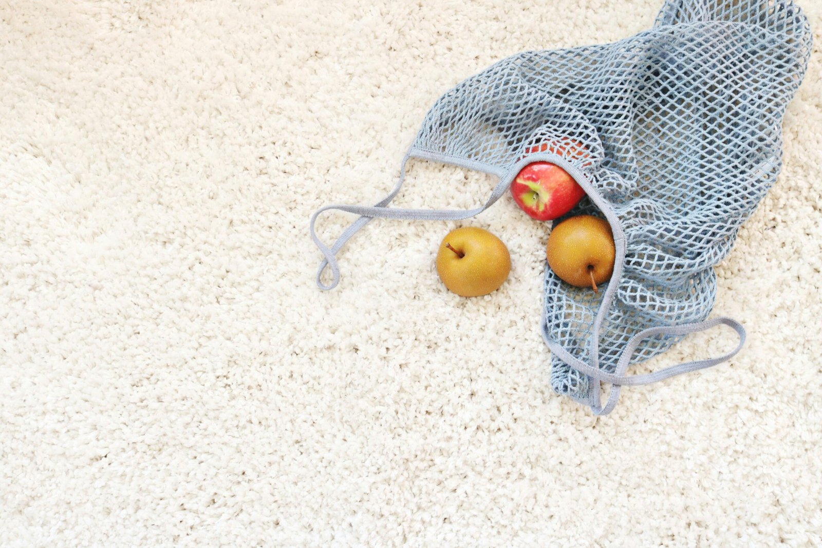 Organic apple and pears in a mesh bag resting on a textured white carpet, symbolizing freshness and sustainability.